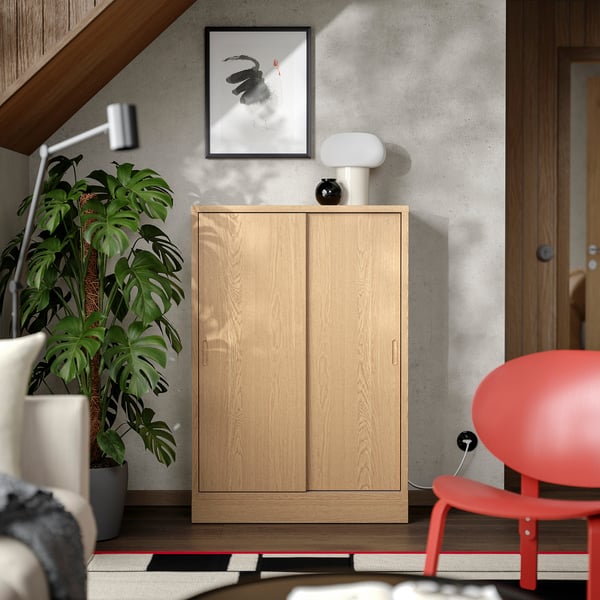 Wooden TONSTAD cabinet with sliding doors, red chair, large plant, modern interior.
