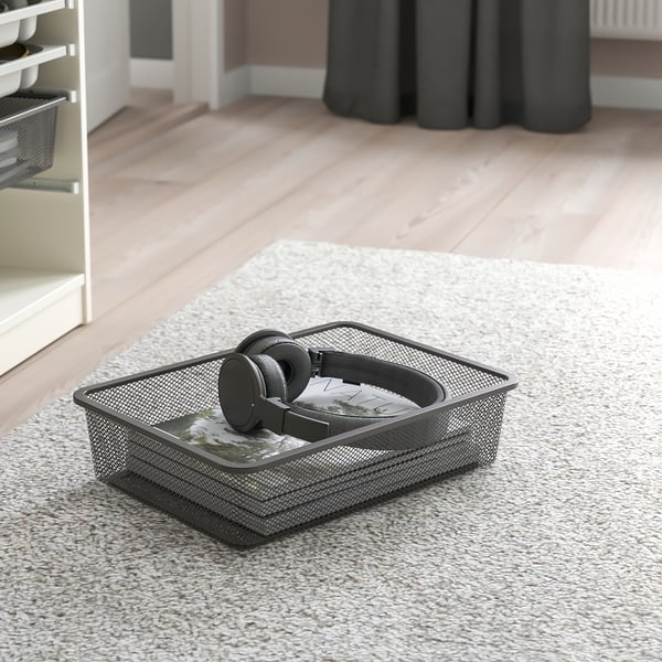 Mesh storage box on carpet, holding headphones and remote, ideal for organising items in the room.
