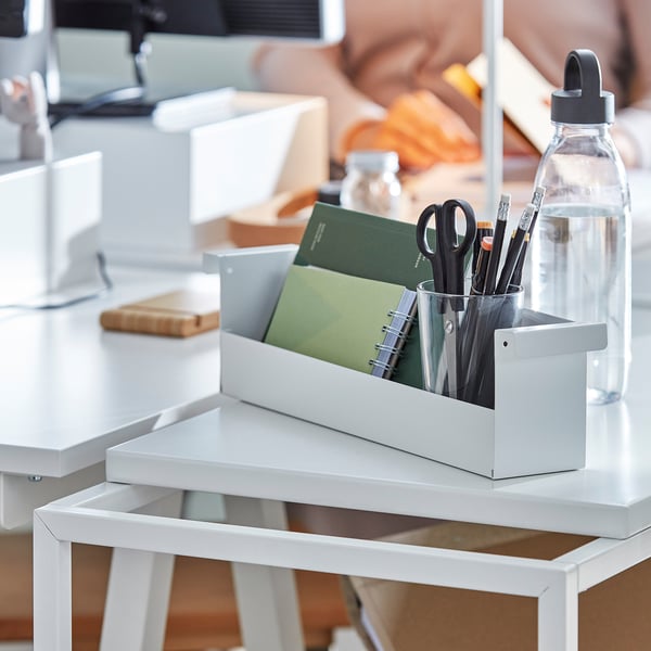 Desk organiser with pens, scissors, notepad, and water bottle.