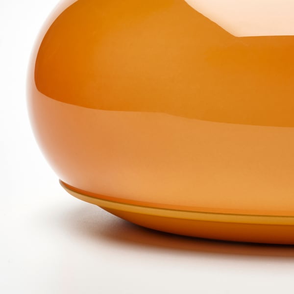 Close-up of modern orange glass lamp, showcasing smooth, curved texture and golden rim.