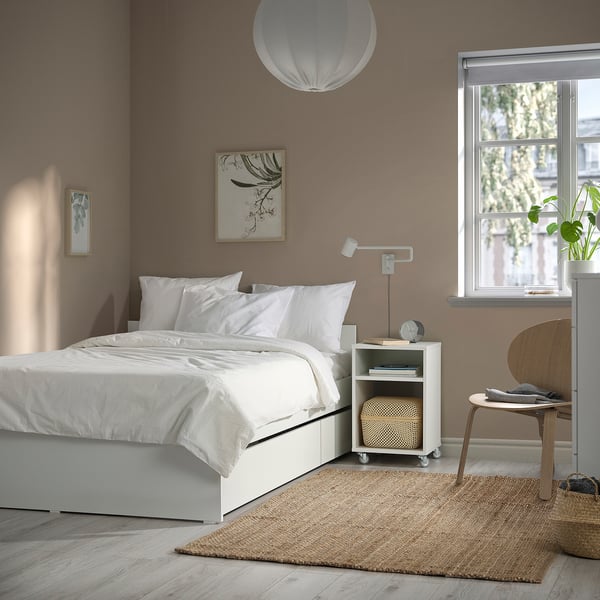 Bedroom with VIHALS white bed frame and 2 storage boxes. Brown walls, white pillows, wooden chair, and plants by window.