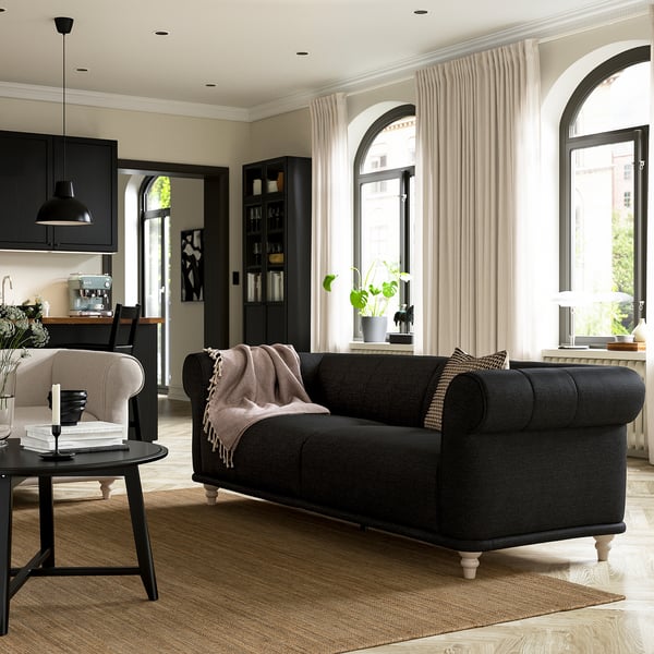 Modern living room with VISKAFORS black sofa, rounded armrests, light curtains, and black kitchen cabinets.