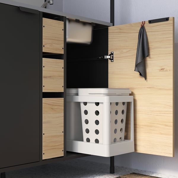 Open kitchen cabinet with pull-out laundry sorter, parted into two white bins with black circles.