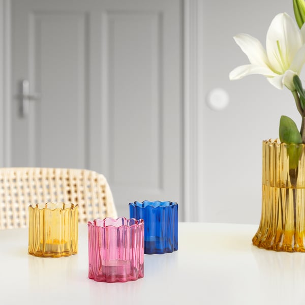 Three colourful tealight holders on a table, with one holding a lit candle, creating a warm ambiance.