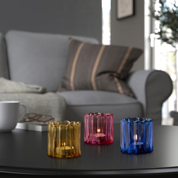 Three colourful glass tealights on table near sofa, festive vibes.