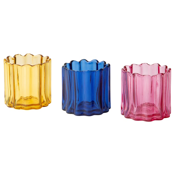 Three colourful tealight holders in yellow, blue, and pink glass. Each has an organic, rippled shape, and they are neatly arranged in a row.
