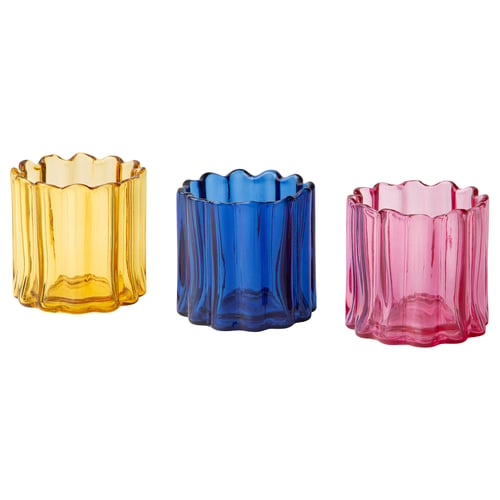Three colourful tealight holders in yellow, blue, and pink glass. Each has an organic, rippled shape, and they are neatly arranged in a row.