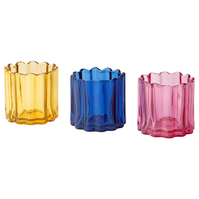 Three colourful tealight holders in yellow, blue, and pink glass. Each has an organic, rippled shape, and they are neatly arranged in a row.