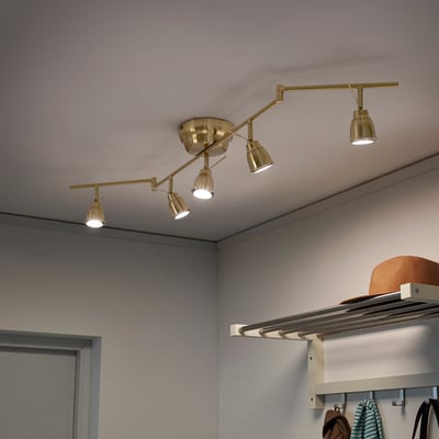 Ceiling track light with adjustable brass arms, five spots directed at different angles, mounted on white ceiling.