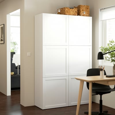 White BESTÅ storage unit in living space, taller than adjacent desk, with woven baskets on top.