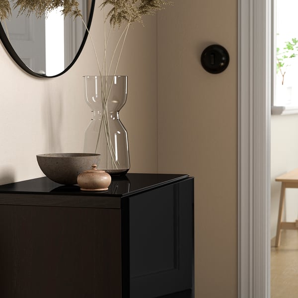 Modern living room with BESTÅ storage, black glass top, minimalist decor, and dried flowers in a vase.