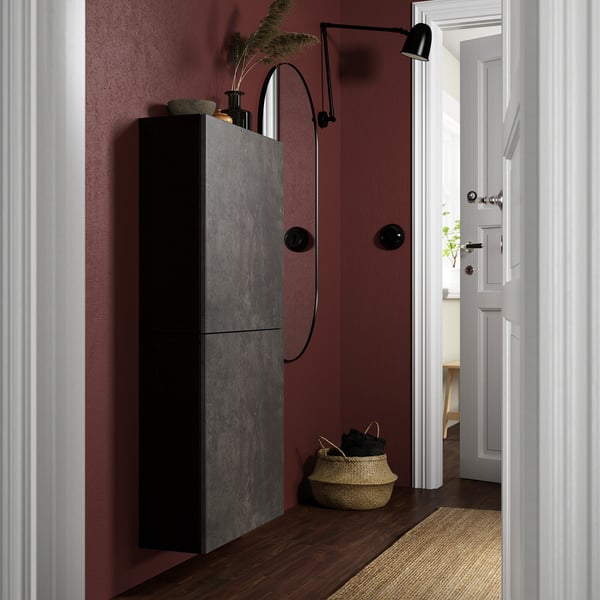 Modern entryway with dark red wall, tall black BESTÅ cabinet, woven basket, and wall-mounted lamp.