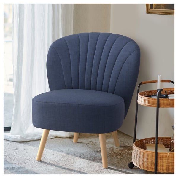 A dark blue BILLHAMN armchair with wooden legs sits by a window, featuring a shell-shaped back and modern, curved design.
