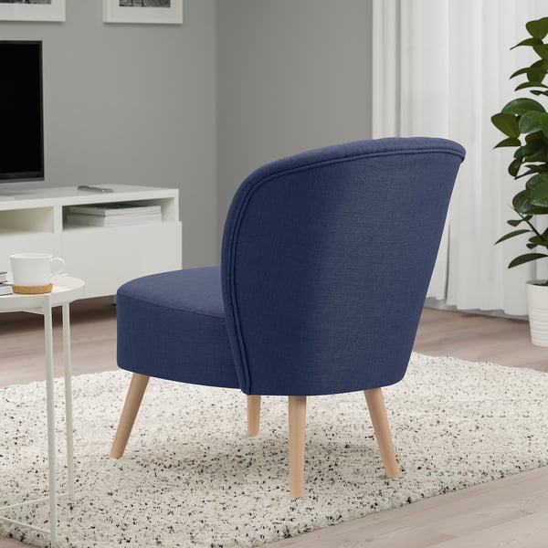 A blue upholstered chair with wooden legs in a living space, providing comfortable seating next to a white table with a cup.