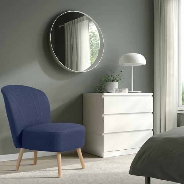 Modern bedroom with blue BILLHAMN chair, white dresser, grey bed, and round mirror. Minimalist decor with clean lines.