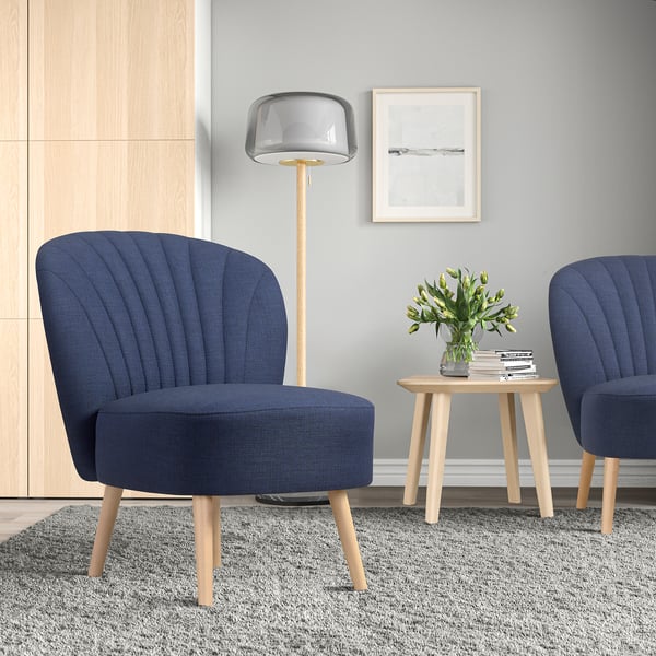 Modern living area with two blue BILLHAMN chairs, a round wooden table with flowers, a grey rug, and a tall floor lamp.