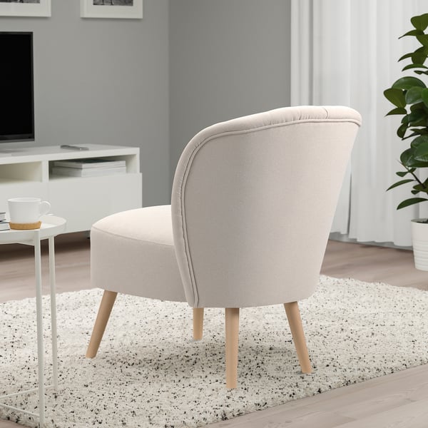 Modern living room with light-colored, curved easy chair on speckled rug by white side table with coffee cup.