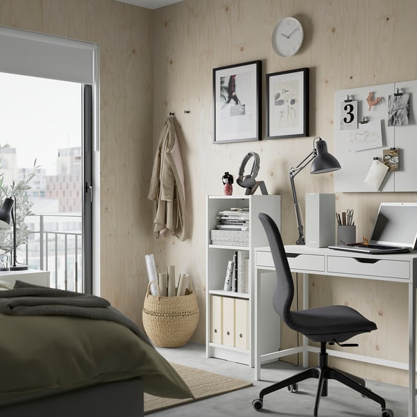 Modern desk setup: chair, laptop, lamp, shelves, wood walls, art, jackets.