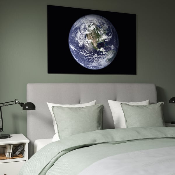 Large earth picture above bed, green frame, canvas material. Headboard and bedding match in colour. Two lamps on nightstands.