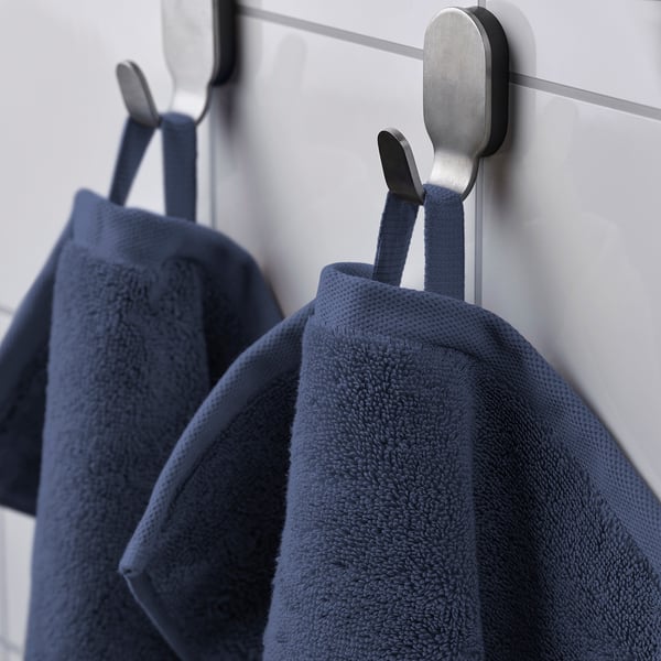 Two blue towels hang neatly on metal hooks against a light wall. The towels feature a textured, absorbent surface and a woven border.