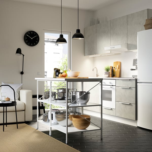 Modern kitchen with ENHET island, pots, bowls, black lights, white walls, striped rug, and chair.