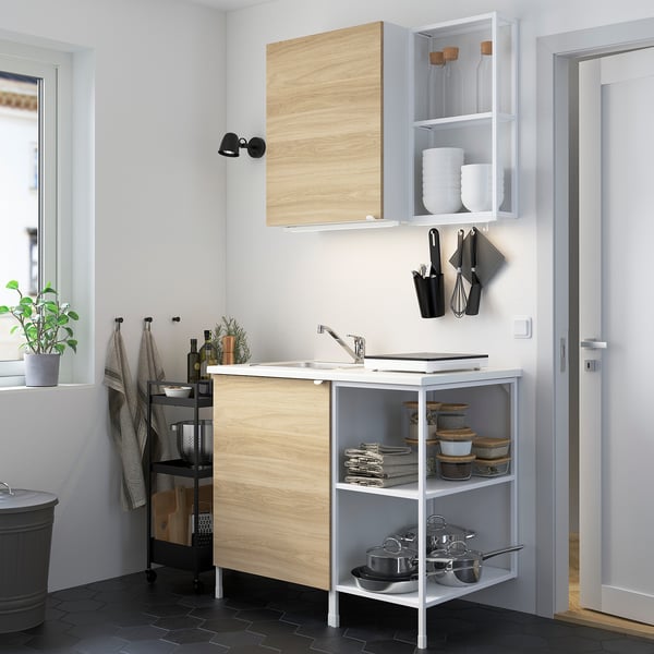 Modern compact kitchen: light wood cabinet, white sink, black accessories, stainless steel sink, compact design.