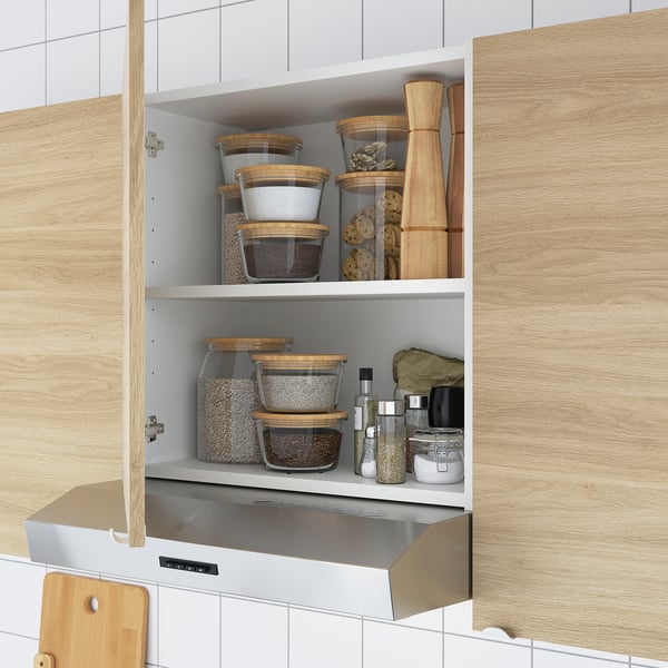 Kitchen cabinet with stacked glass containers and wooden lids, holding dried foods and wooden utensils.