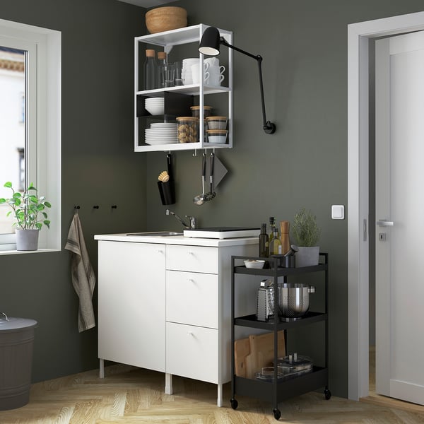 Modern kitchen with white ENHET cabinets, black accessories, and green walls. Includes sink, induction hob, metal trolley, and wall shelves.