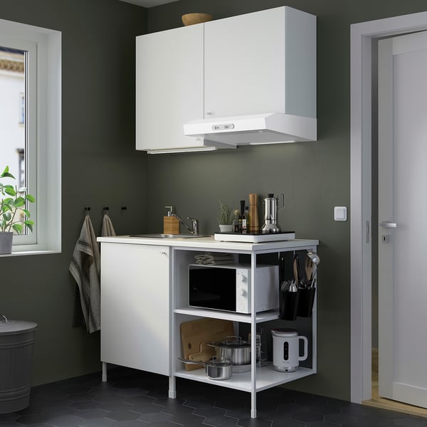 White ENHET kitchen unit with sink, shelves, microwave, kettle; green wall; small space efficient.