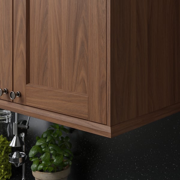 Brown wooden kitchen cabinets with metallic handles and a potted plant on the dark countertop. The deco strips enhance the kitchens aesthetic.