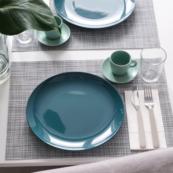 Table set with teal FÄRGKLAR plates, cutlery, and glasses on grey placemats.