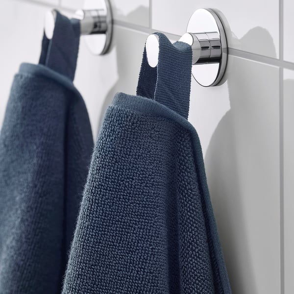 Two blue towels hang on chrome rail, secured, against white tiles.