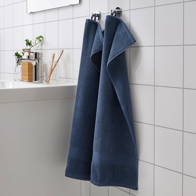Dark blue FREDRIKSJÖN towel hangs large on tiled wall, near sink with accessories.