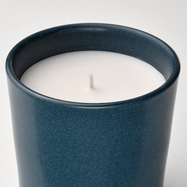 Close-up of a dark green stoneware candle holder with a white wax candle. The wick is unlit and centred.