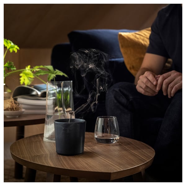Person on couch with wine, table has candle, water, books.