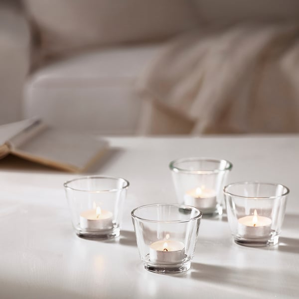 Four small lit tealights in clear glass holders on a table, creating a warm, cosy ambiance.