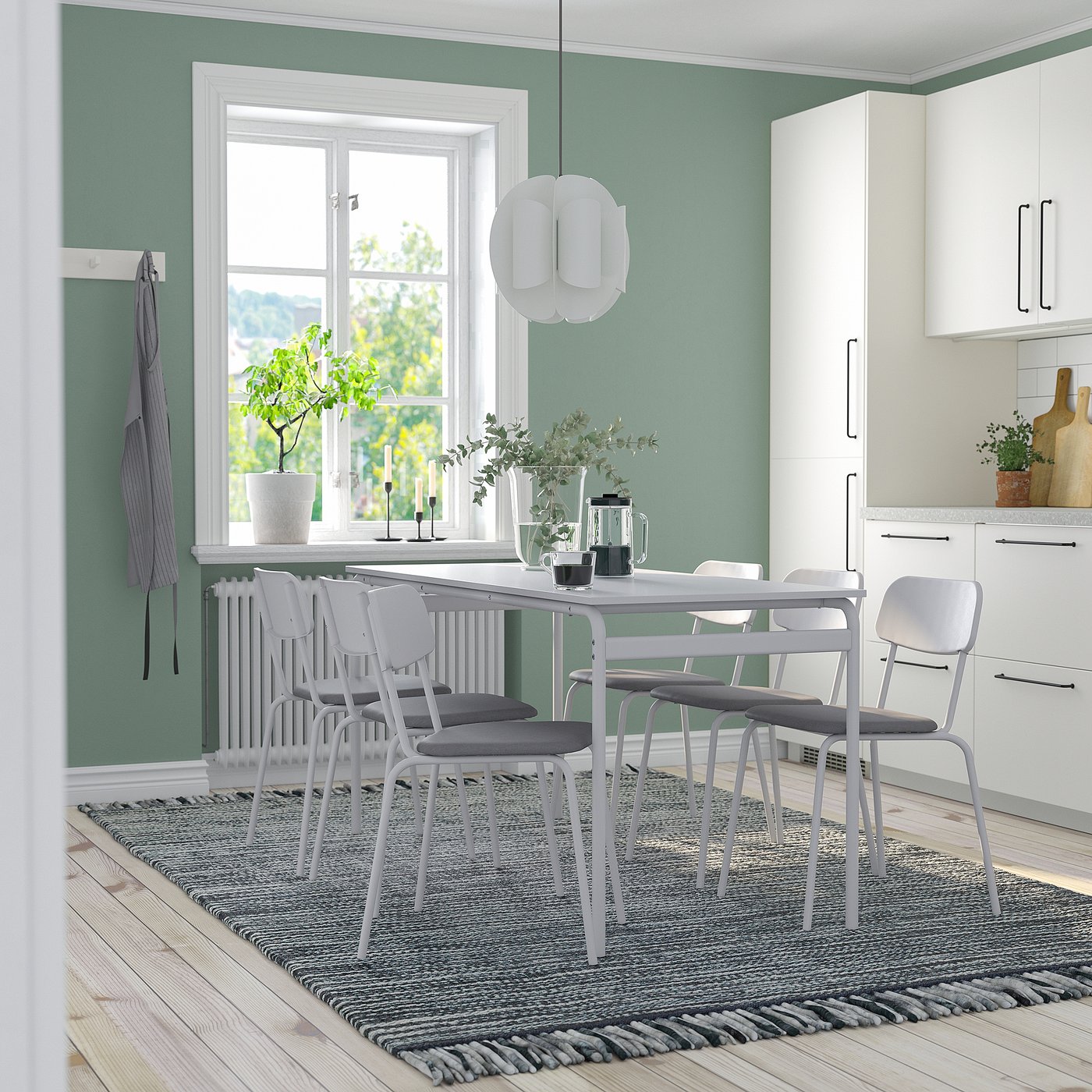 Modern dining room with white table, grey chairs, and green wall. Pendant lamp, wooden floors, and rug.