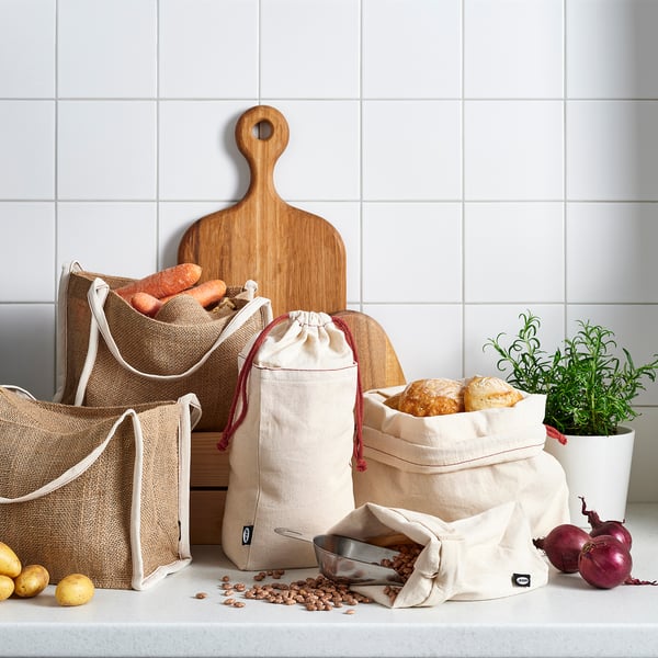 Textile bags in beige holding food, cotton, ideal for baked goods & veggies. Wooden board & greenery visible.