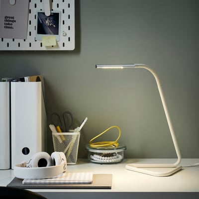 Modern minimalist desk setup with HÅRTE white led lamp, headphones, scissors, pens, and other stationery. Lamps slim design fits well among items.