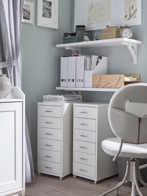 Well-organized home office with white HELMER drawer units on wheels. Multiple drawers, shelves, and a grey swivel chair. Grey walls and wooden floor.