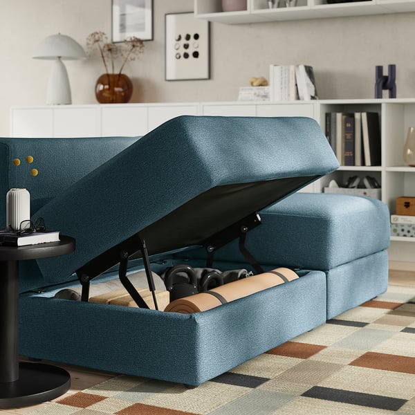 Blue JÄTTEBO sofa with open storage underneath, showing yoga mat and shoes. Soft, modular design with easy-to-access storage for multiple items.