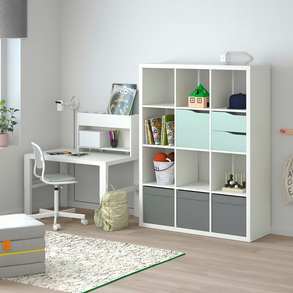 Modern kids study setup with KALLAX shelving unit featuring door inserts, holding books, toys, and desk with chair.