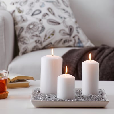 Three candles on tray with glass, in front of sofa.