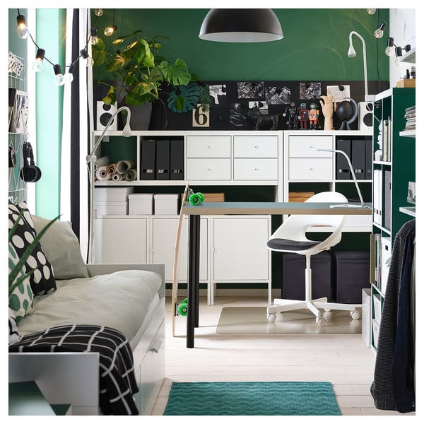 Modern home office with white desk, chair, green rug, string lights, and plants.
