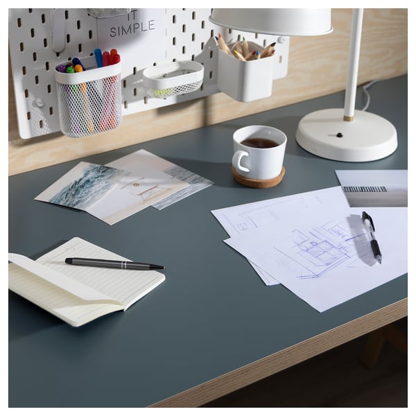 Organised workspace: grey desk with white lamp, notebook, sketches, photos, mug, pens. Pegboard with organisers.