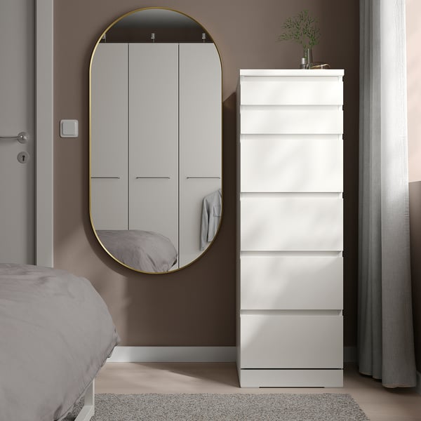 LINDBYN gold oval mirror beside dresser, reflecting room, minimalist decor.