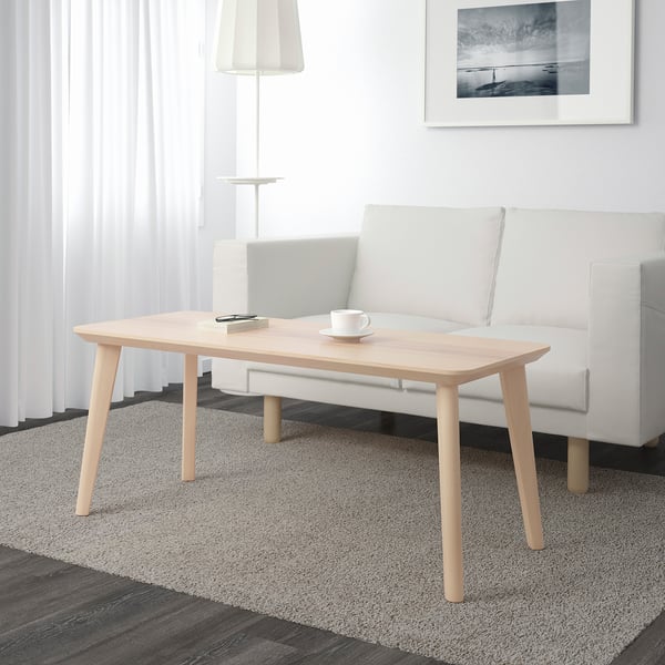 Minimalist living room with wooden coffee table, mug, notepad. Grey sofa, lamp, striped rug.