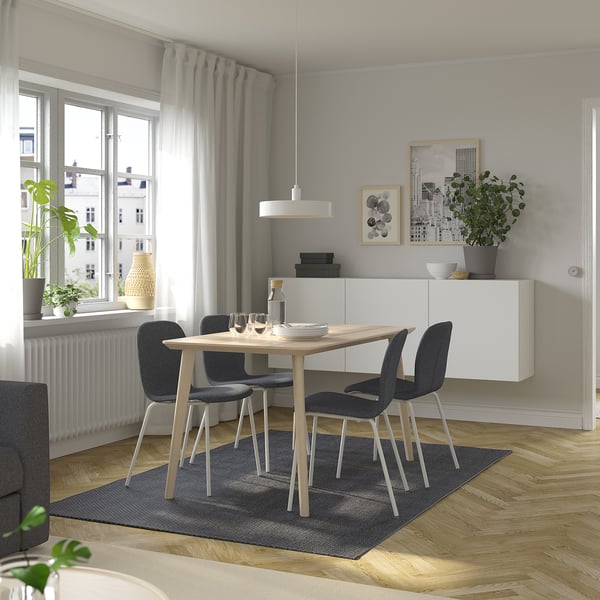 Modern dining set with light wood table, grey chairs, blue rug, pendant light, and window curtains.