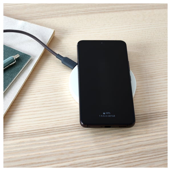 Wireless charging smartphone at 55% on pad beside book.