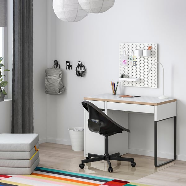 Modern home office with a white MICKE desk, black chair, and colourful rug. Pegboard with accessories and decorative lanterns.